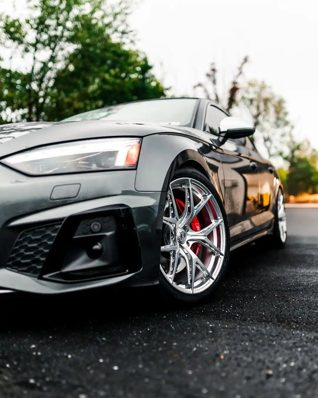 A dark gray Audi with polished chrome multi-spoke wheels and red brake calipers.