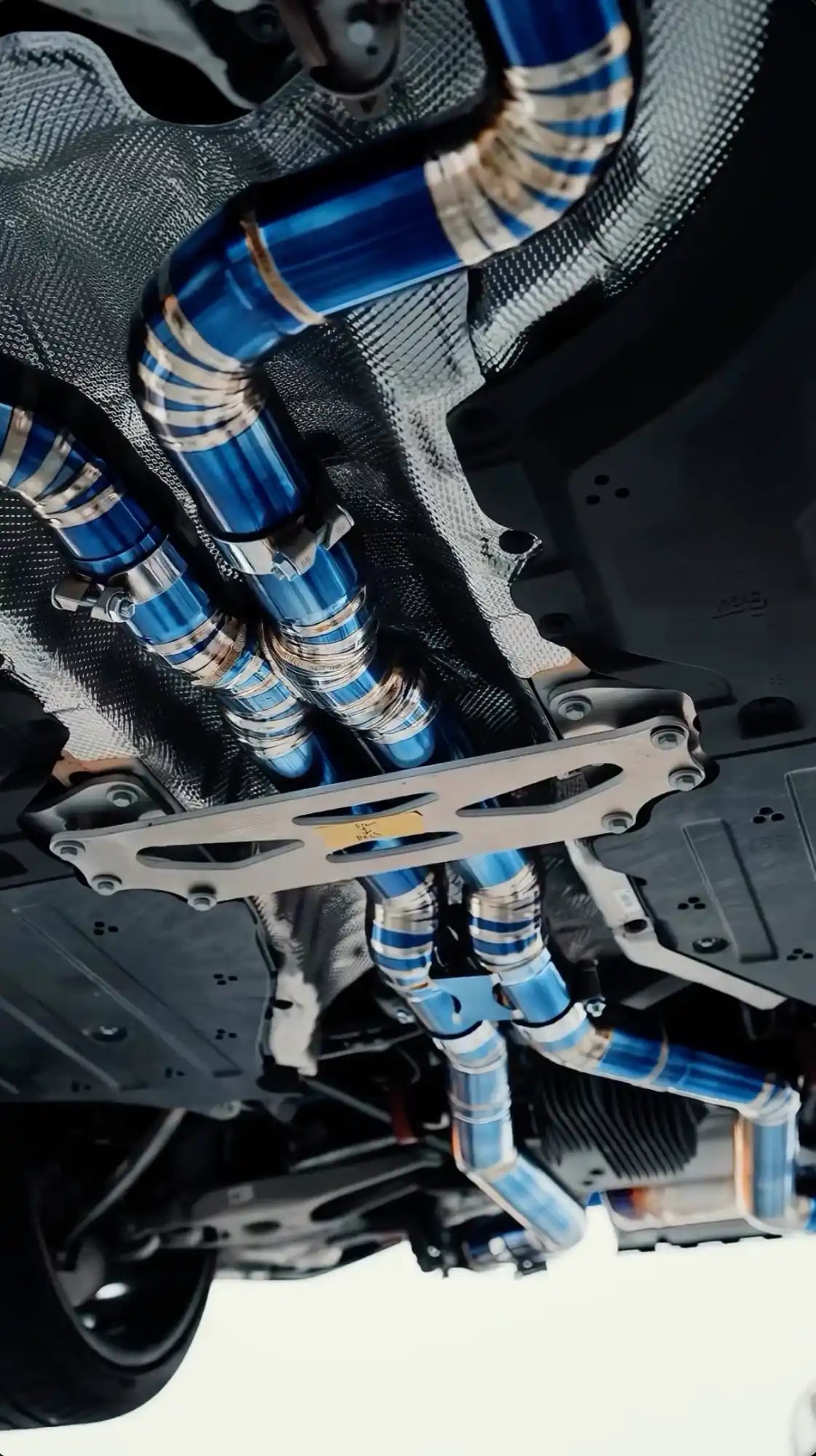Undercarriage view of a vehicle’s blue and silver exhaust system with a silver brace.